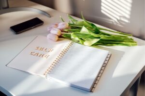 Soul Healing Aufgeschlagenes Kalender, Handy und Tulpen liegen auf dem Tisch. Auf dem Kalender steht "self care" geschrieben